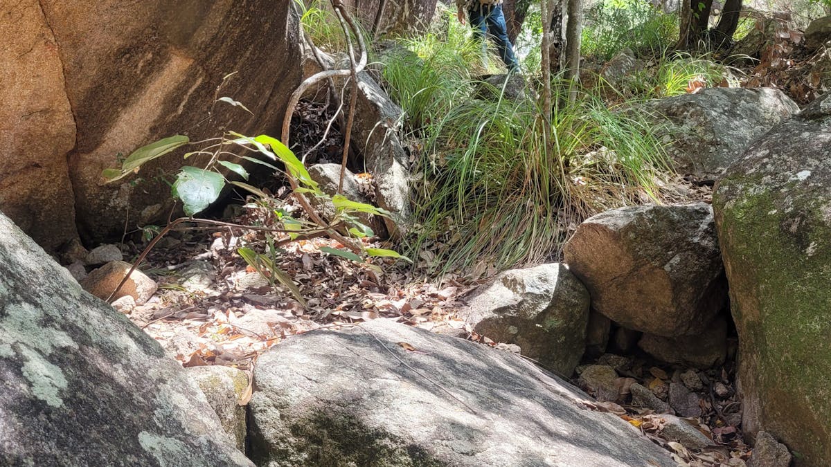 Yellow arrow in black circle marker attached to rock on left-hand side. Person standing in distance. Yellow arrow in black circle marker attached to rock on left-hand side. Person standing in distance.