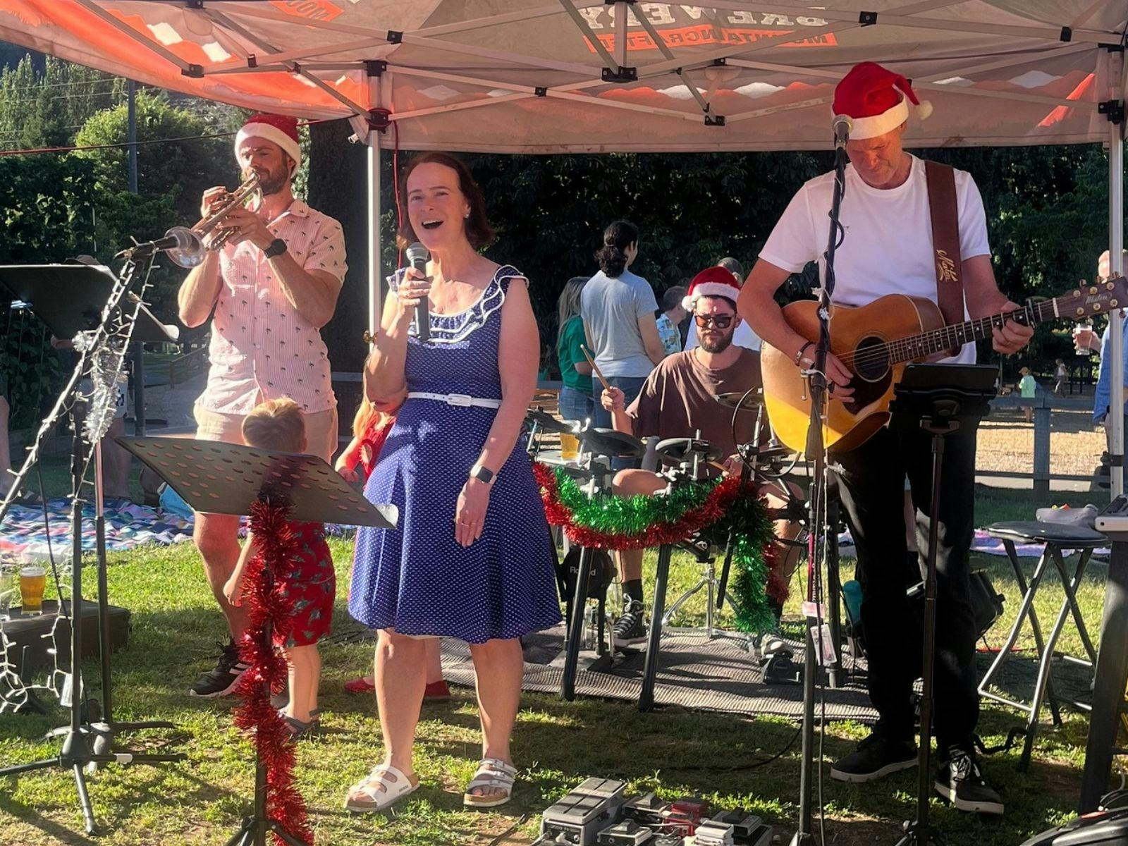A lady singing carols with two musicians in an outdoor setting at Bright Brewery Paddokc