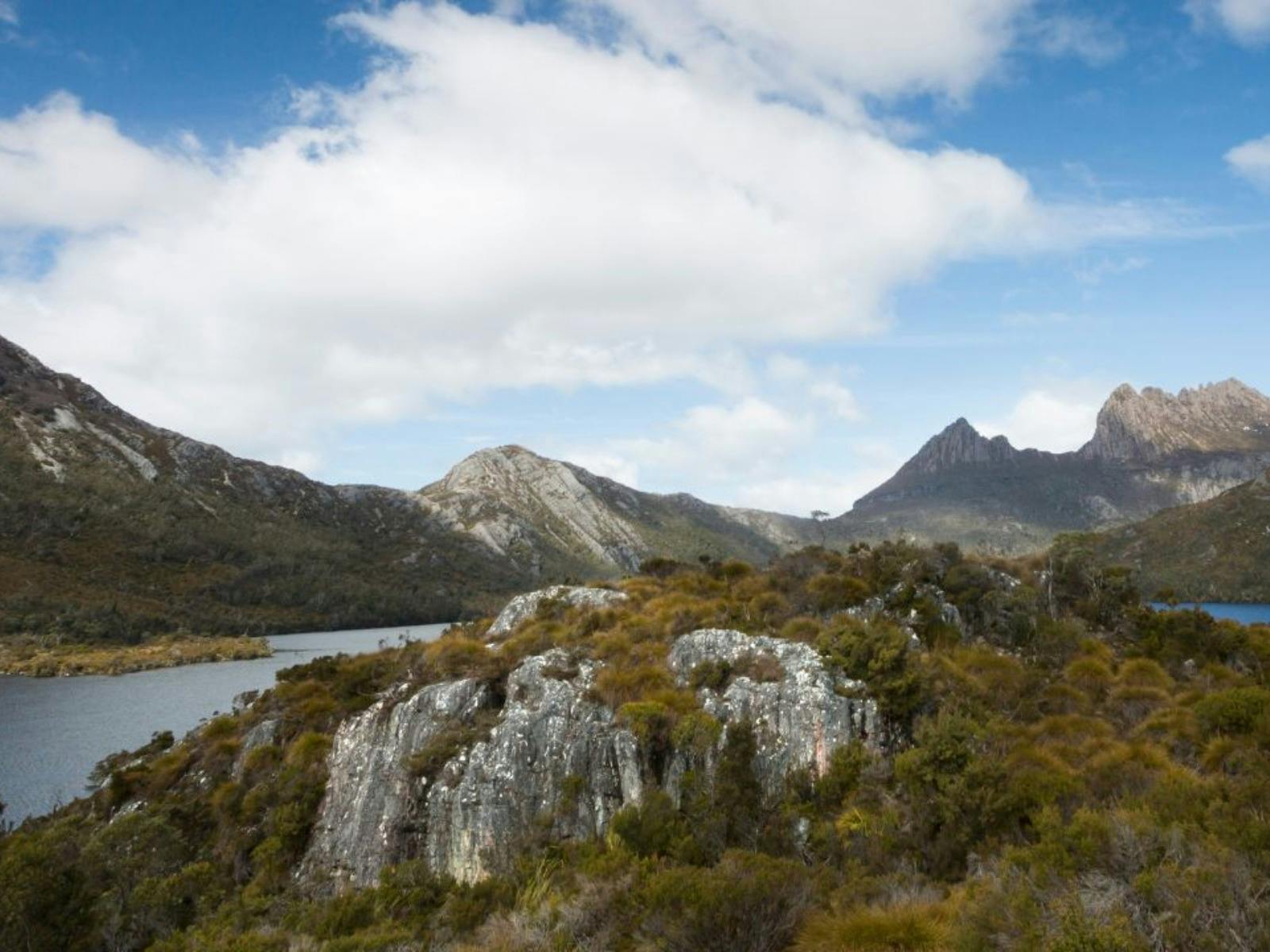 Craggy mountains and hills surrounding a dark lake under a bright, cloudy sky.
