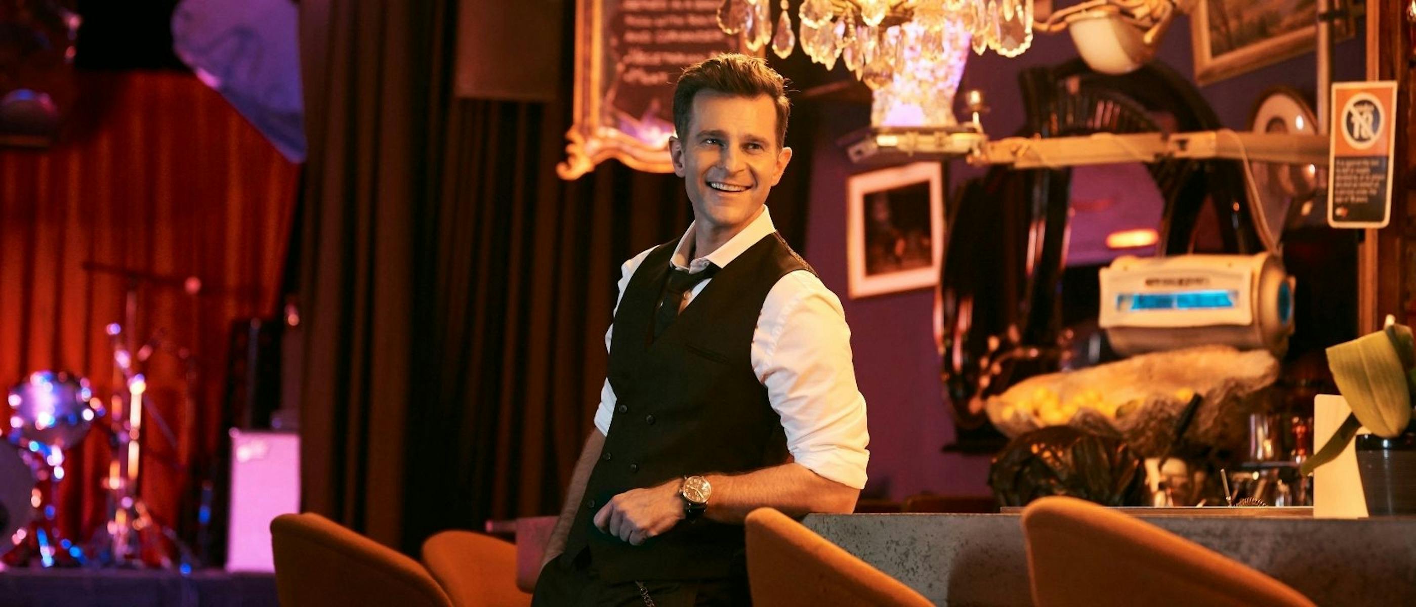 David wearing a suit and smiling. There is a stage behind him.