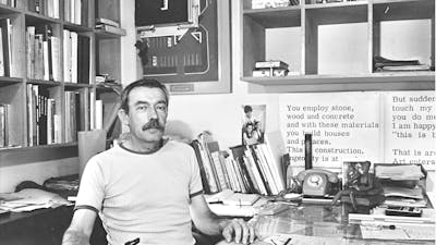 Enrico Taglietti holding a pen at his desk in his studio, photo taken in 1985