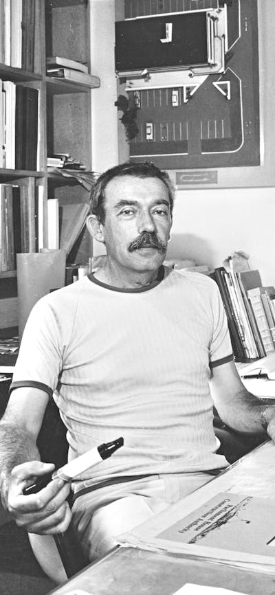 Enrico Taglietti holding a pen at his desk in his studio, photo taken in 1985
