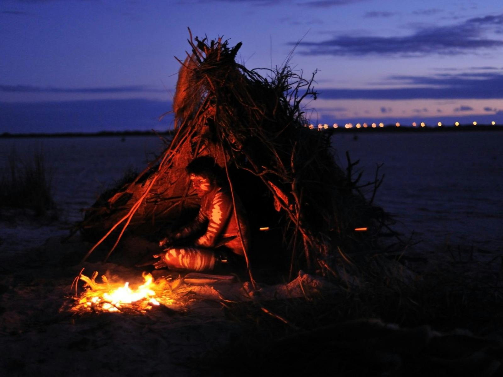 Man tending to fire within a shelter.