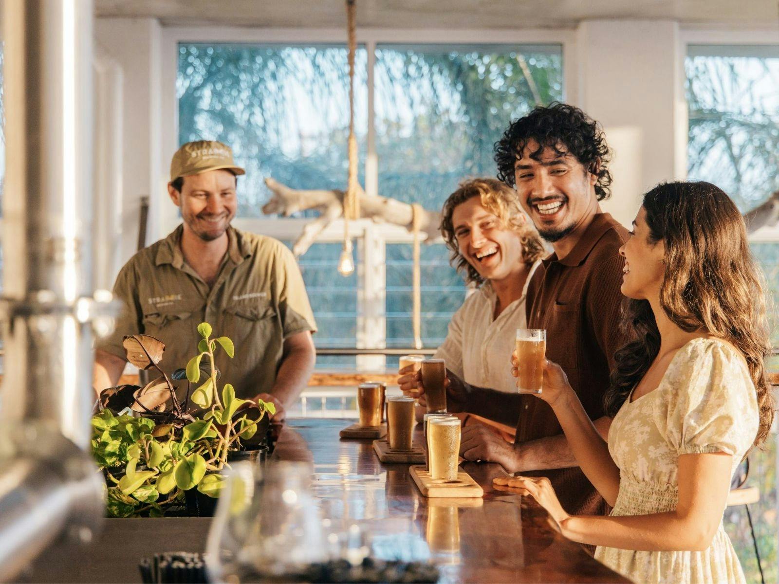 3 people stand at a bar tasting beer, fourth person to the side