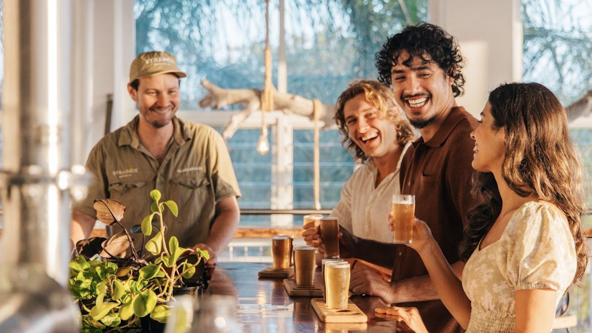 3 people stand at a bar tasting beer, fourth person to the side