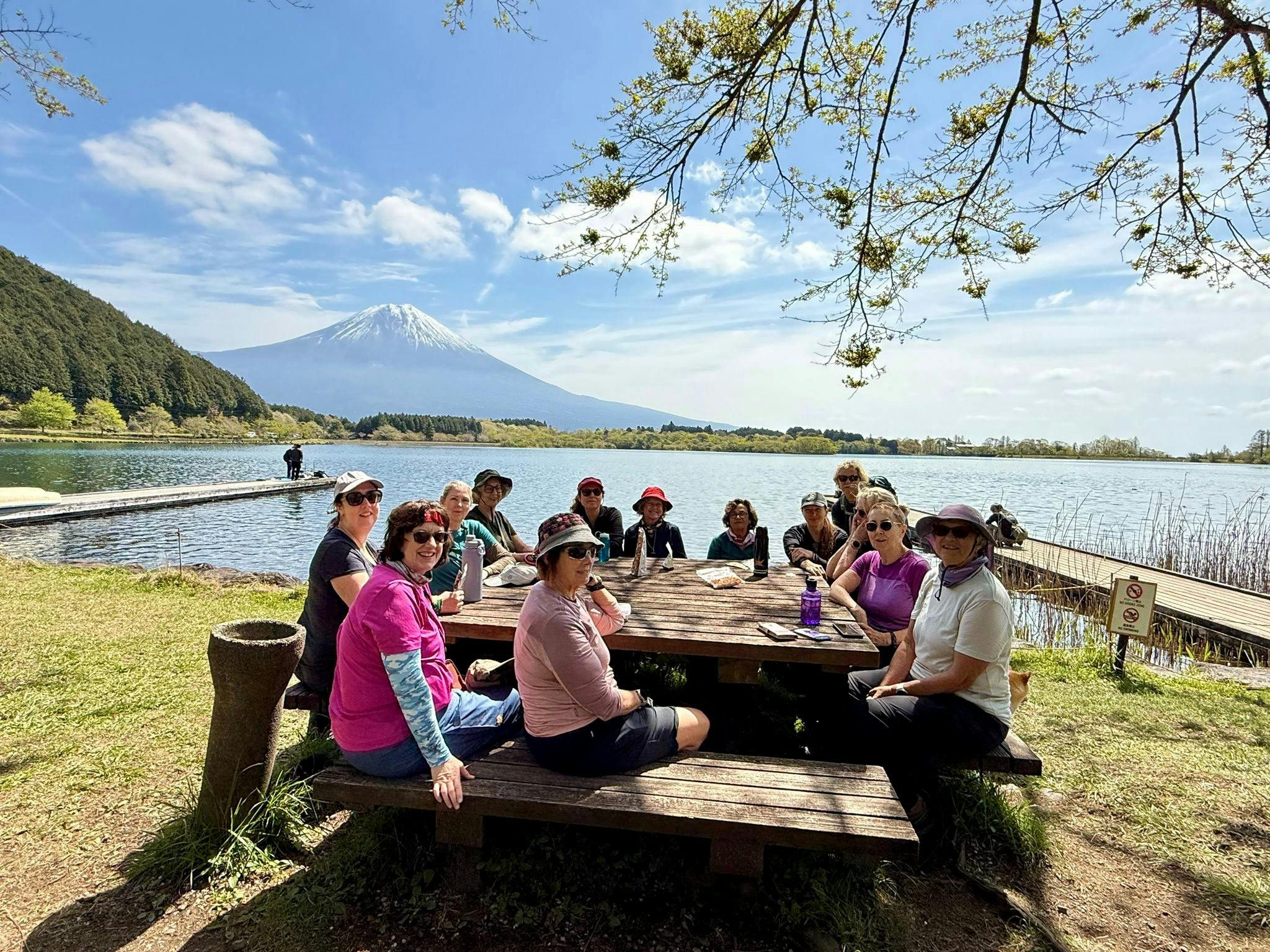 Women hikers sitting around a table alongside a lake at the base of Mt Fuji in Japan.