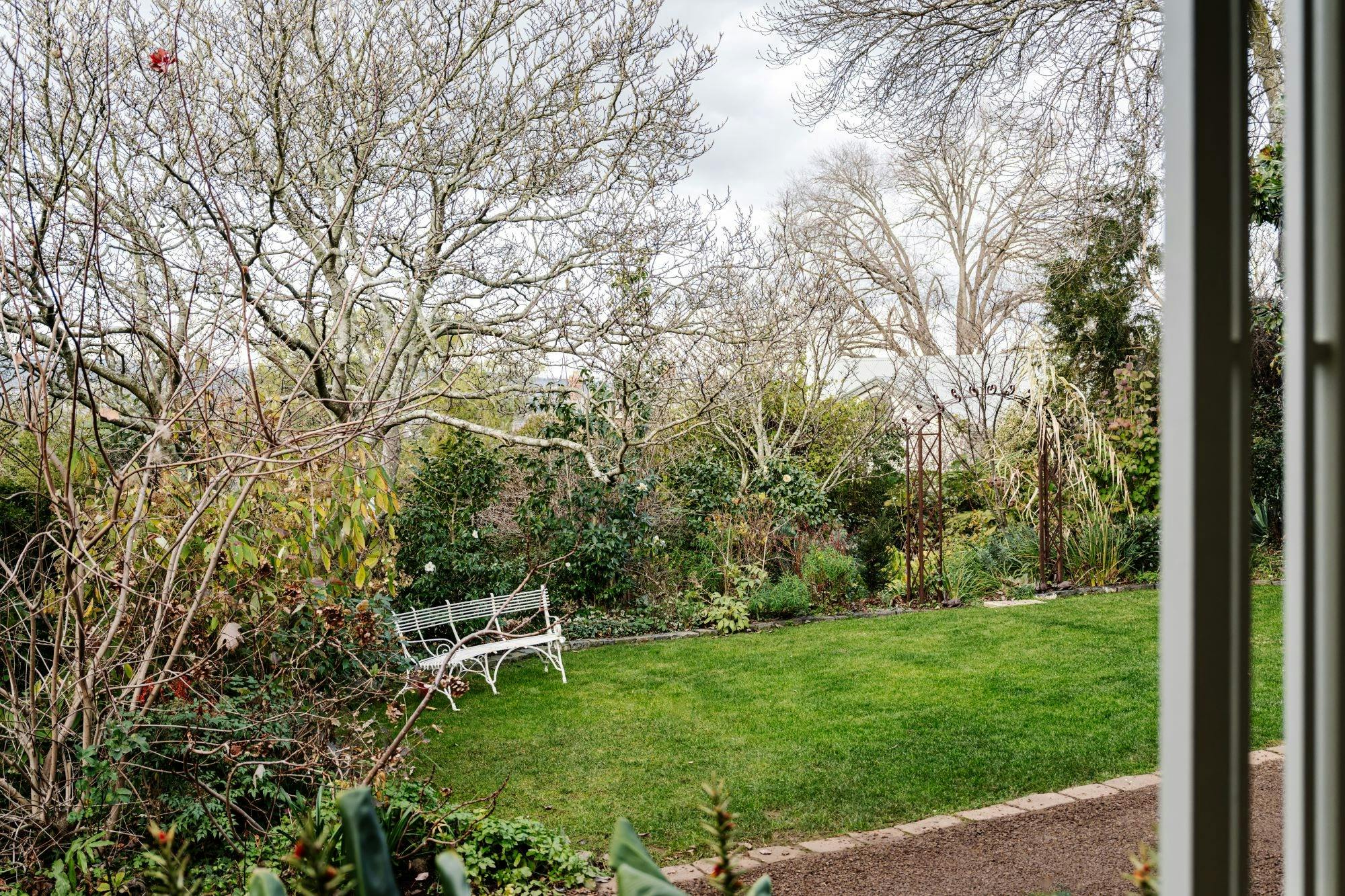 A green and lush lawn with a bench seat in an enclosed and private garden setting.
