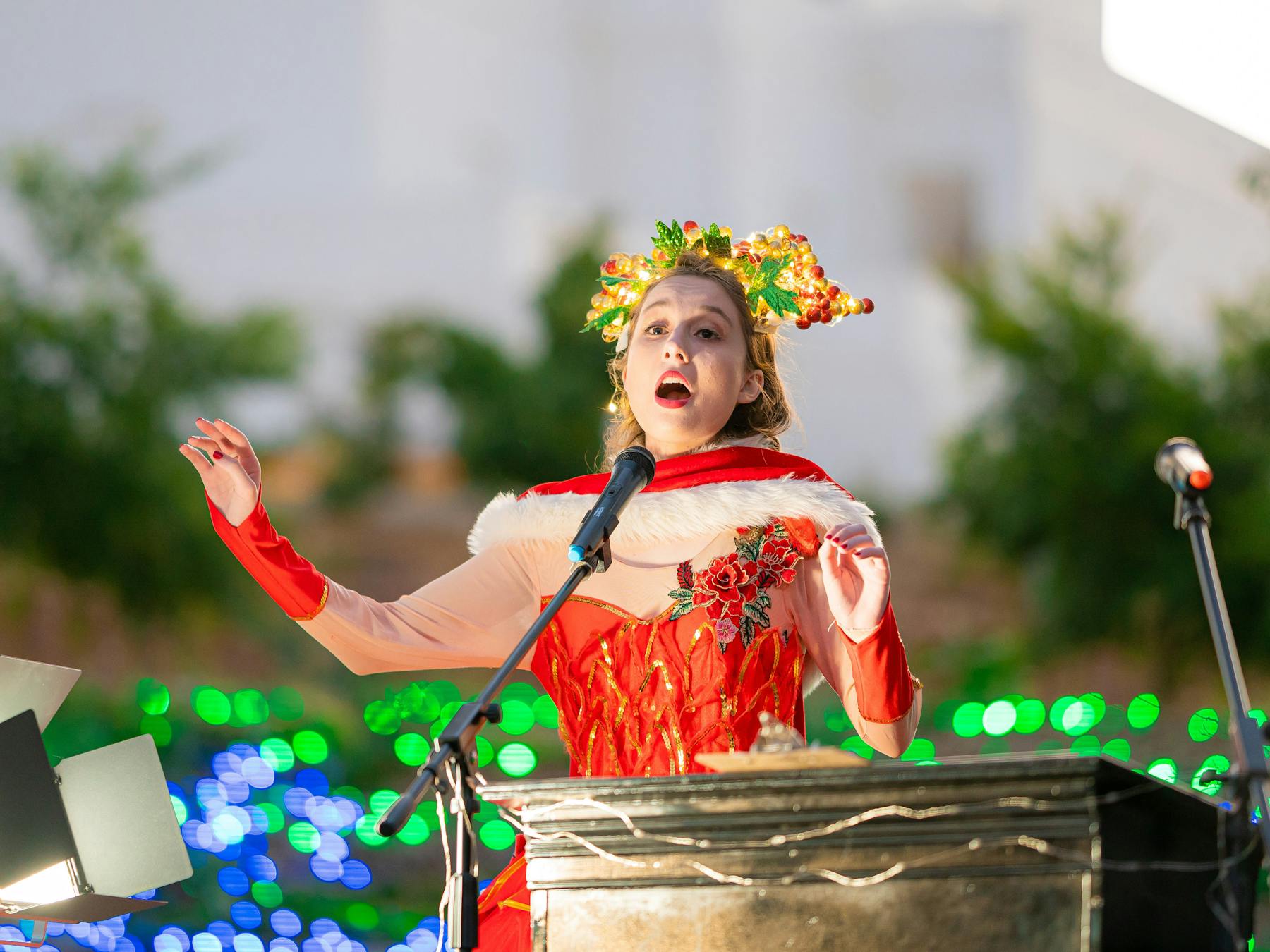 Opera singer in christmas dress singing into a microphone with hands raised