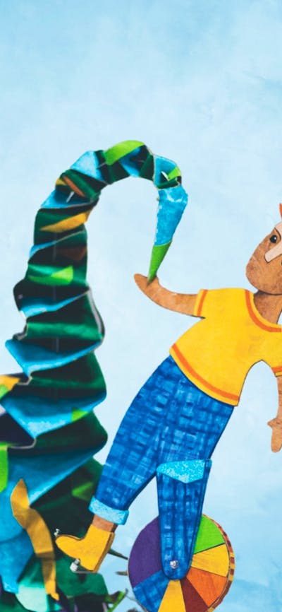 A paper cutout person stands on a mound of folded colourful paper