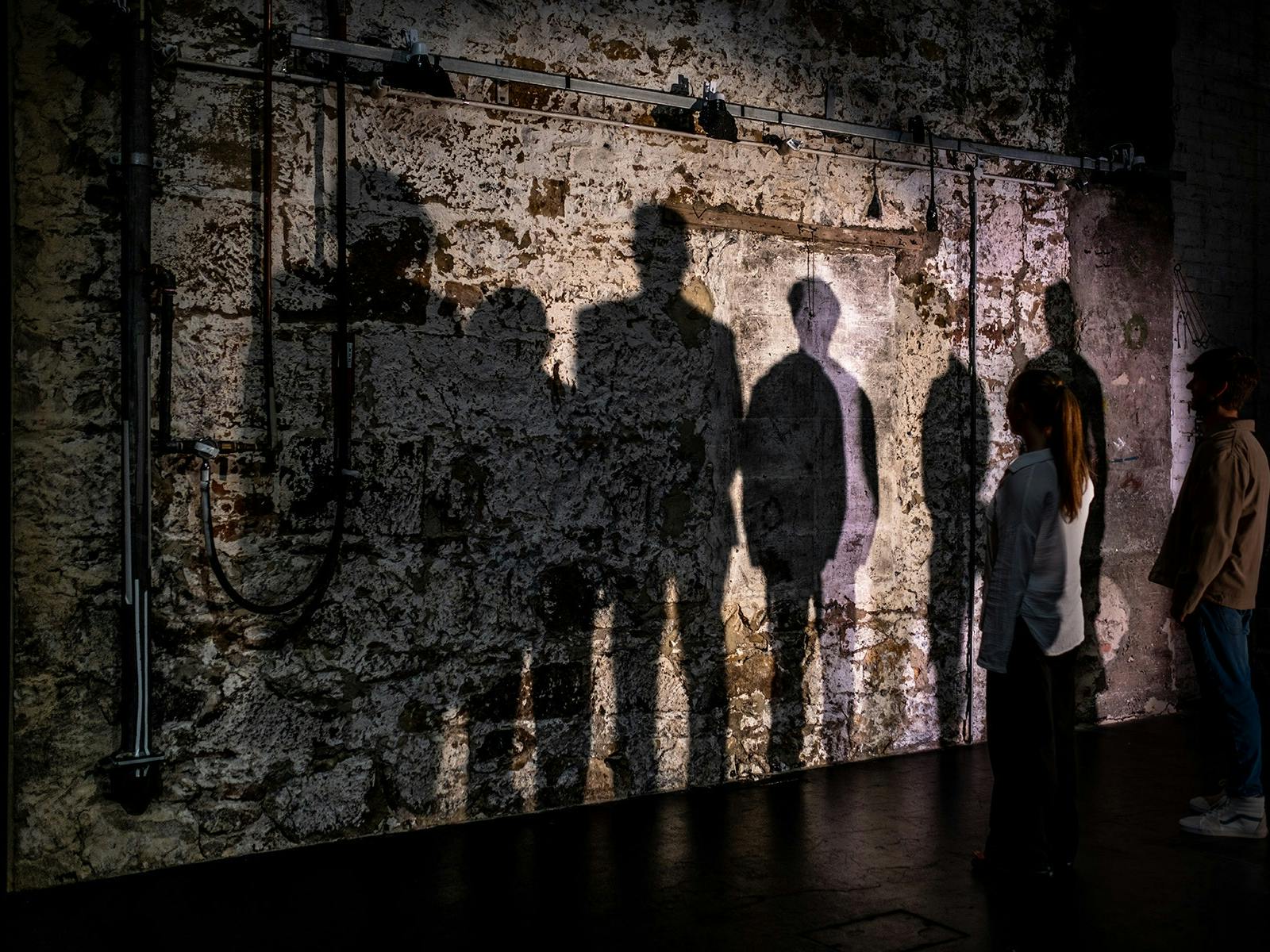 Shadows from a group of people are cast against an old sandstone wall