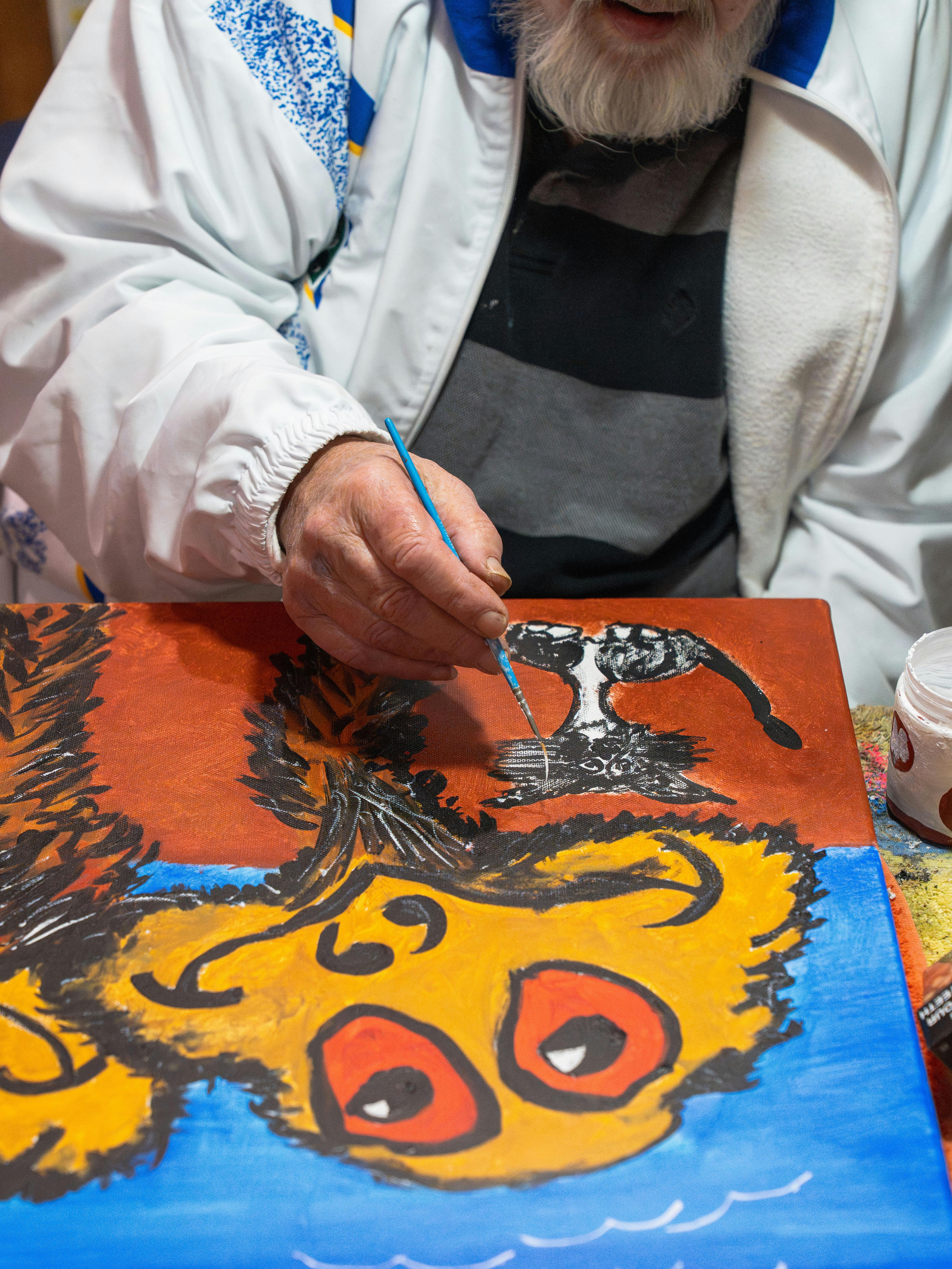 Older artist painting a colourful Emu Brothers artwork featuring two expressive emus.