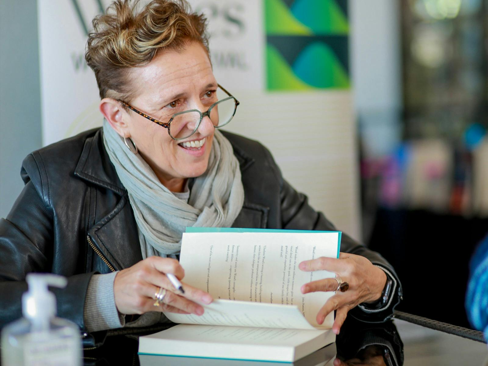Charlotte Wood holds a book open as she signs it, smiling at someone off screen