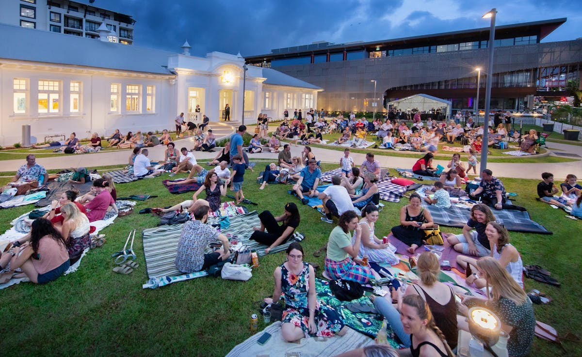 People sitting on the grass outside The Court House watching live music