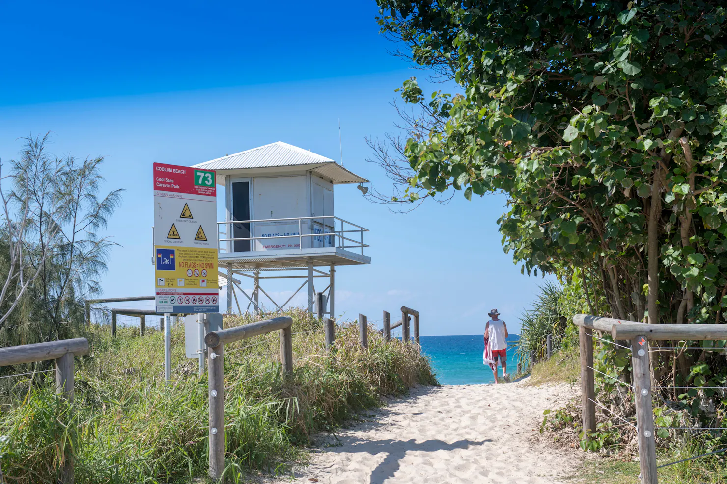 Image of Coolum Beach access from caravan park with man on beach and surf watch house to the left