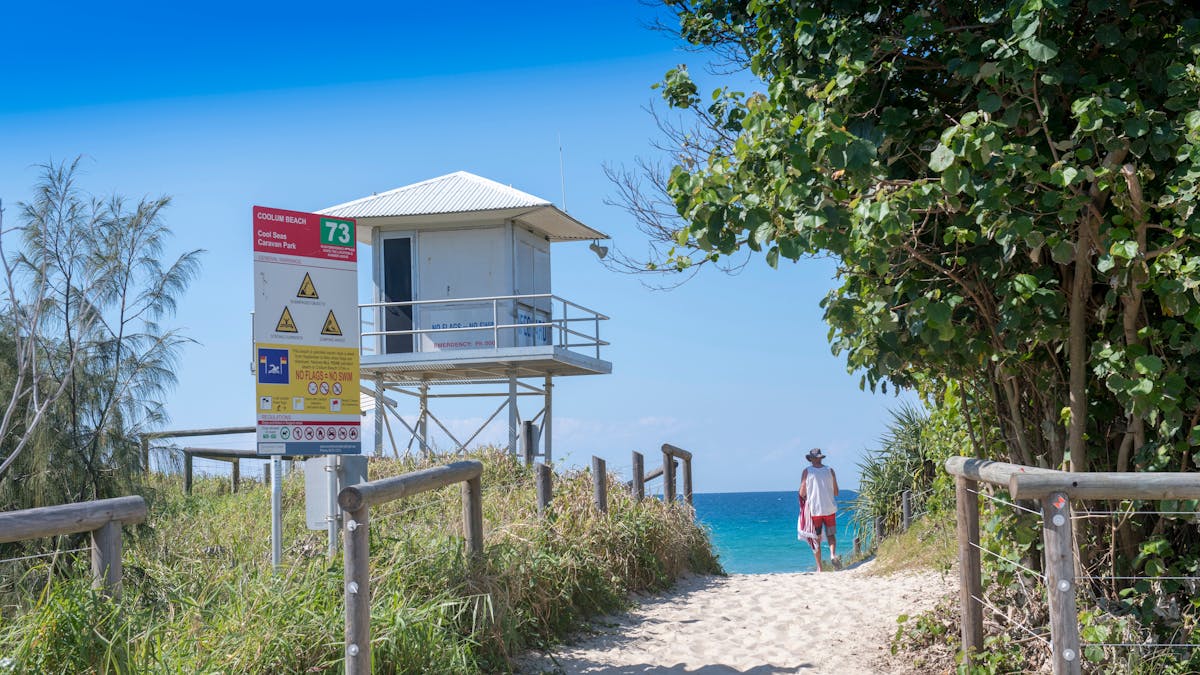 Image of Coolum Beach access from caravan park with man on beach and surf watch house to the left