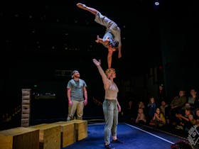 An acrobat is doing a one handed handstand on another's head