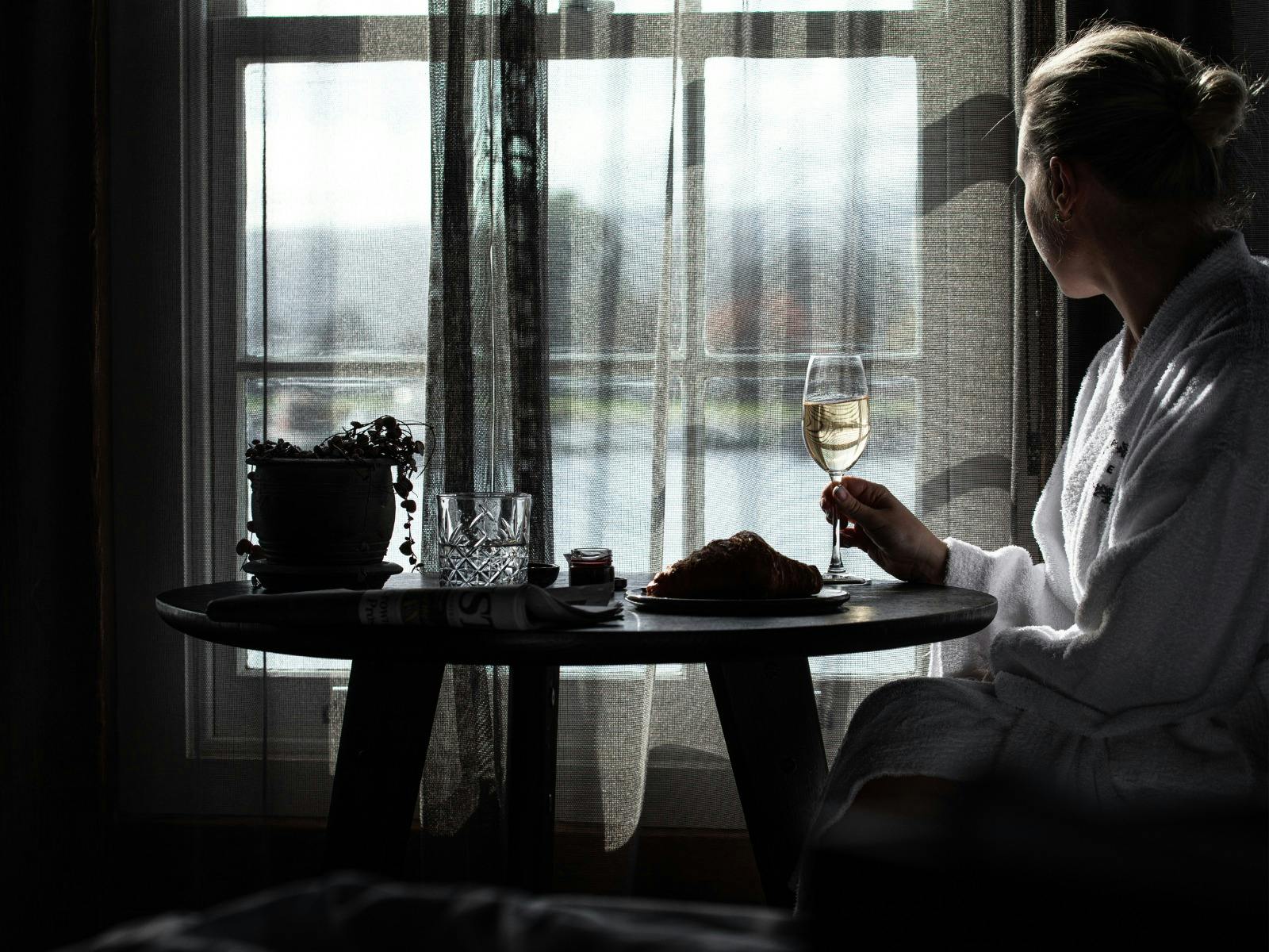 A person sitting a table looking out the window at the water