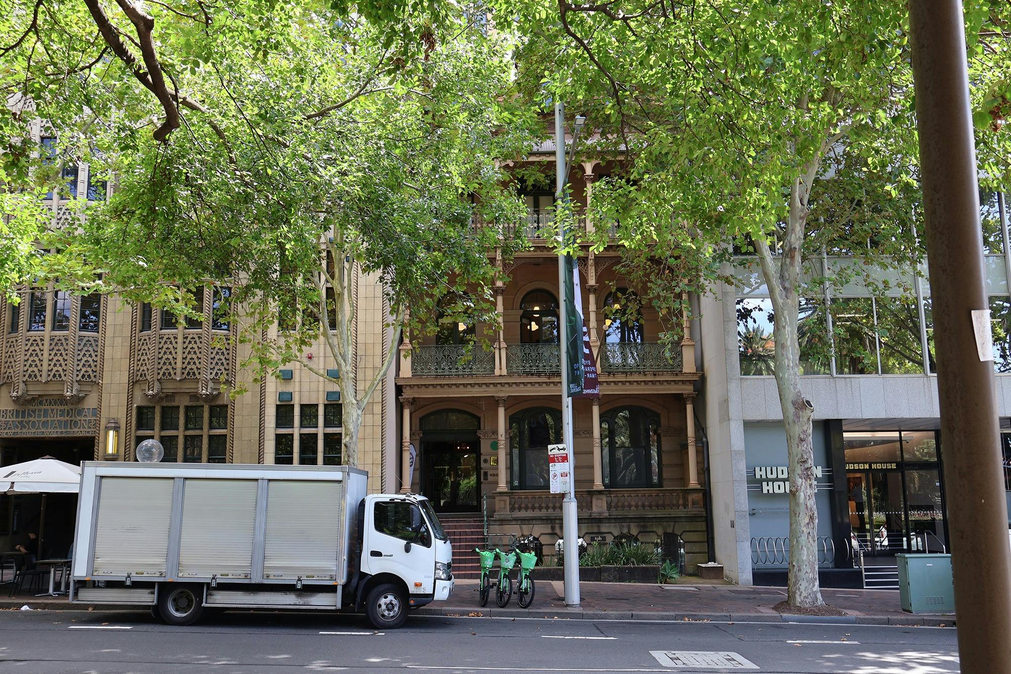 A building seen from across the street with trees and a white truck parked in front of it