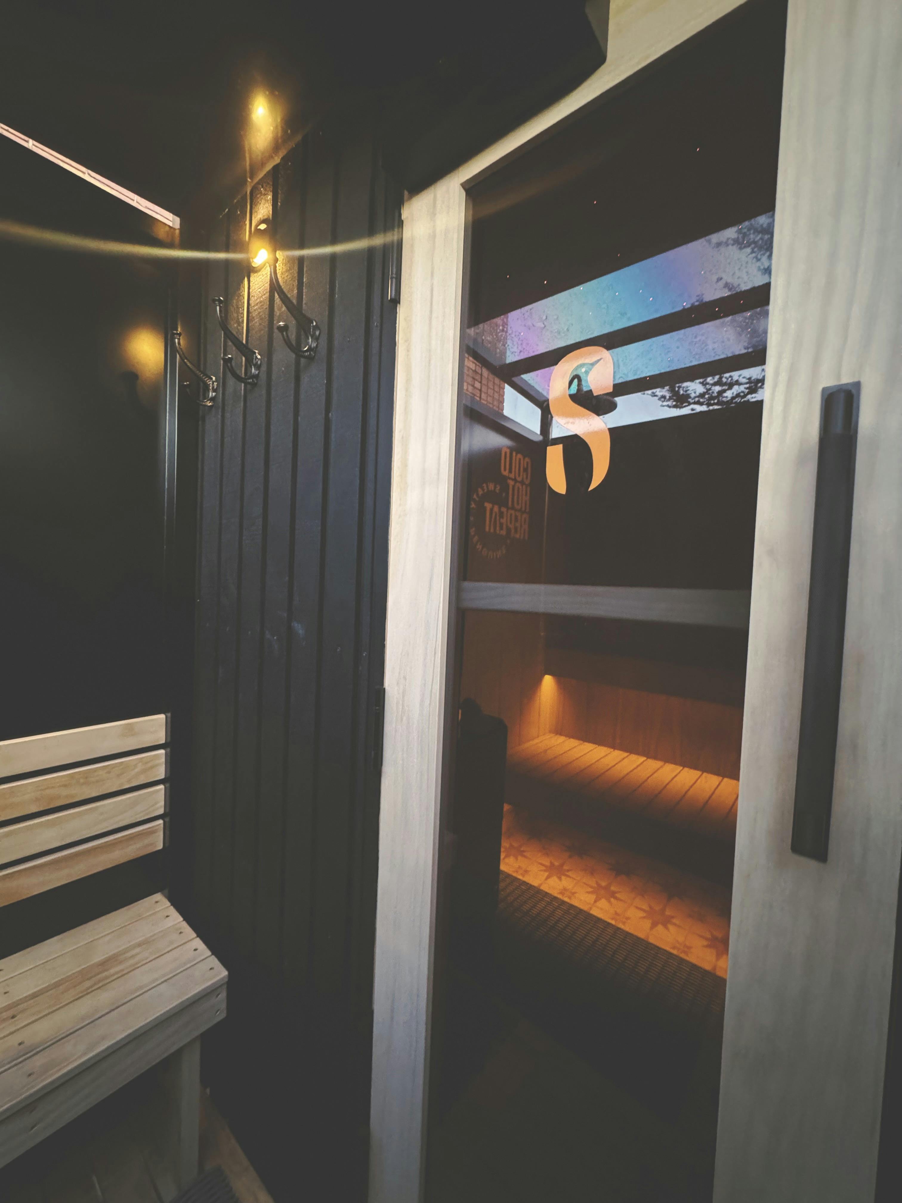 Sauna entrance showing the S logo on the glass door and warm interior lighting.