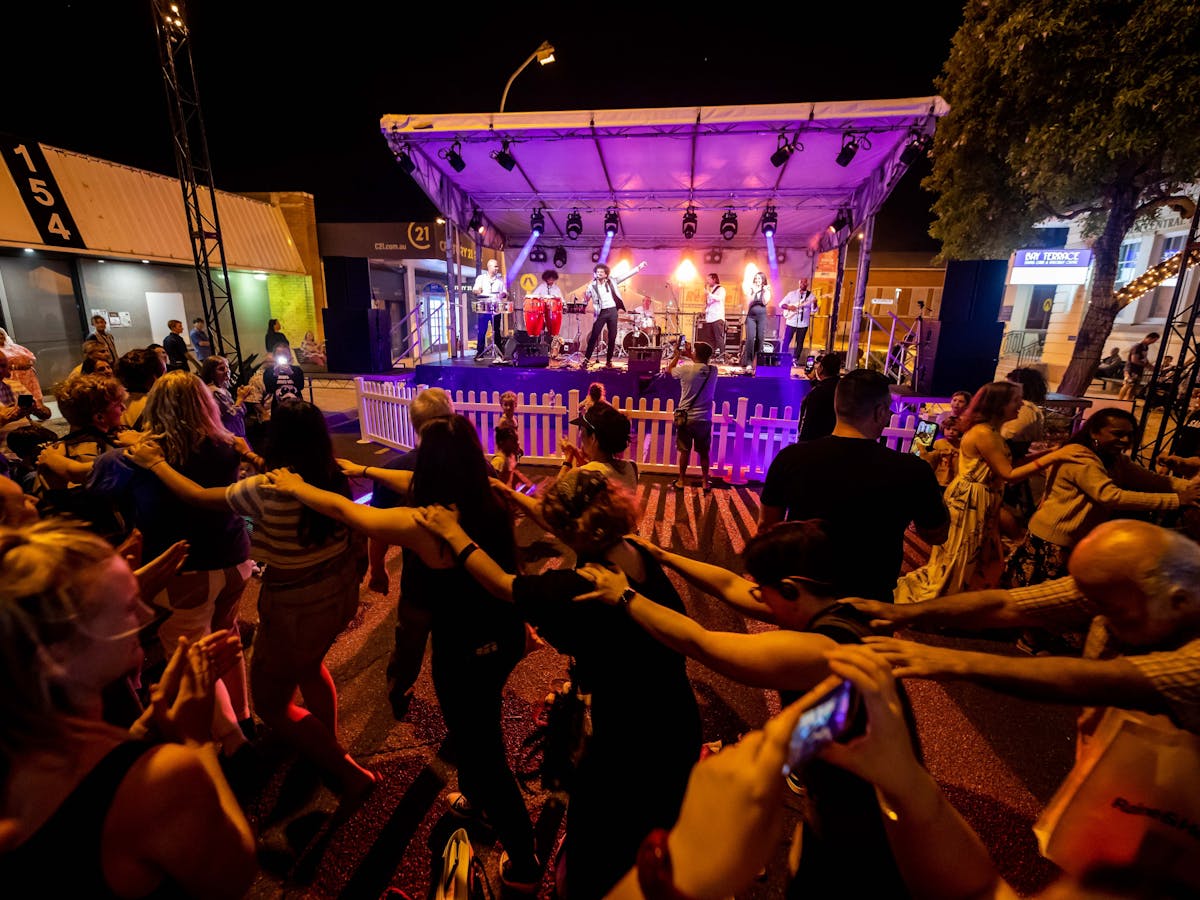 People dancing in front of a stage with their arms linked
