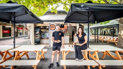 Two Cafe Cultura workers standing outside of the cafe, holding plates of food.
