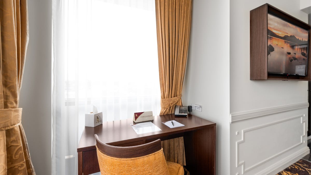 Luxury King Suite desk setting featuring a fabric chair, wooden desk, curtains at the window and TV
