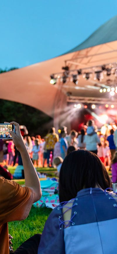 People sitting on grass, looking up at stage as they watch outdoor performance