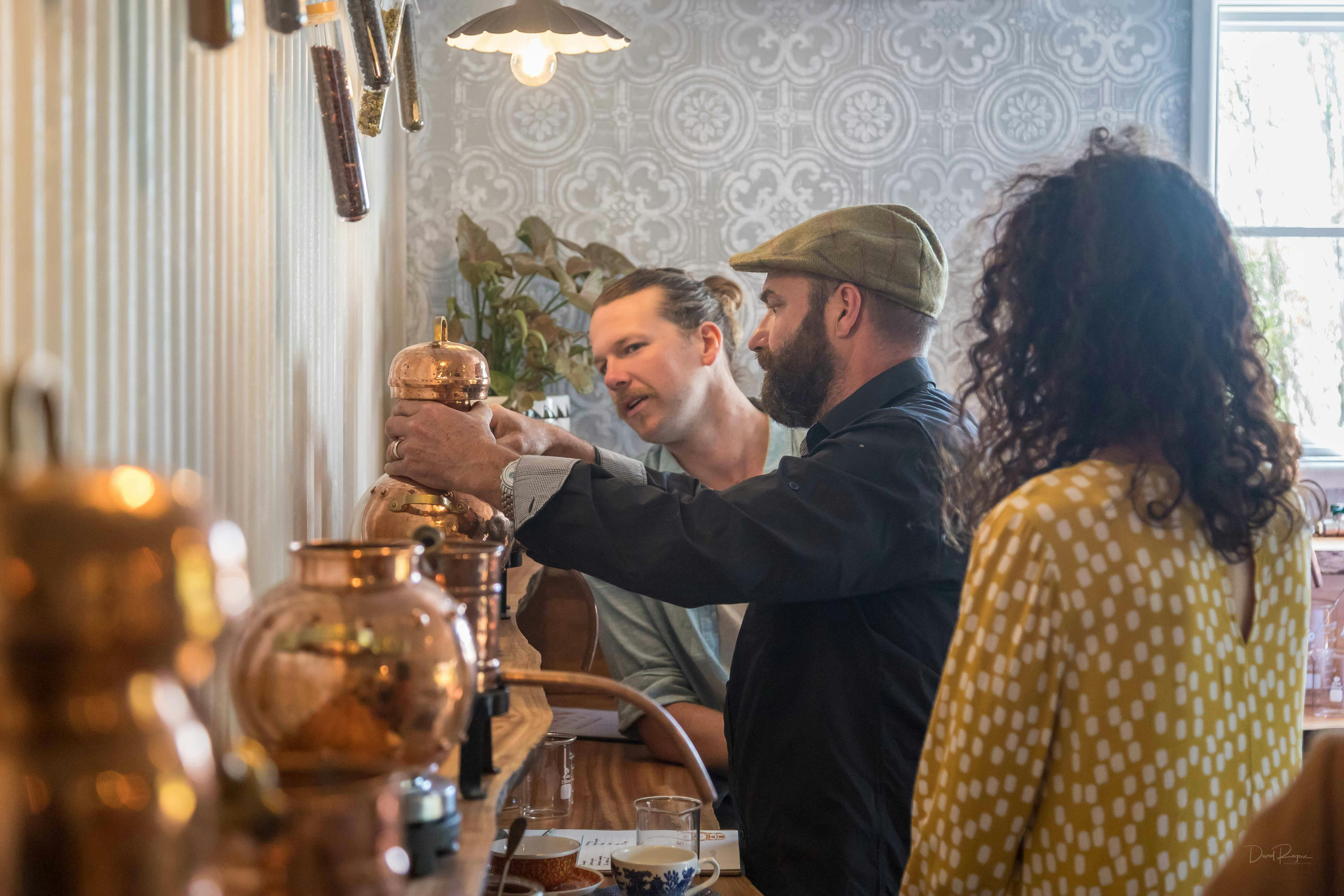 Three people working at a still on a bench with copper stills in the foreground