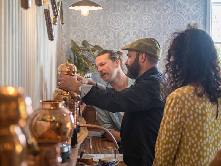 Three people working at a still on a bench with copper stills in the foreground