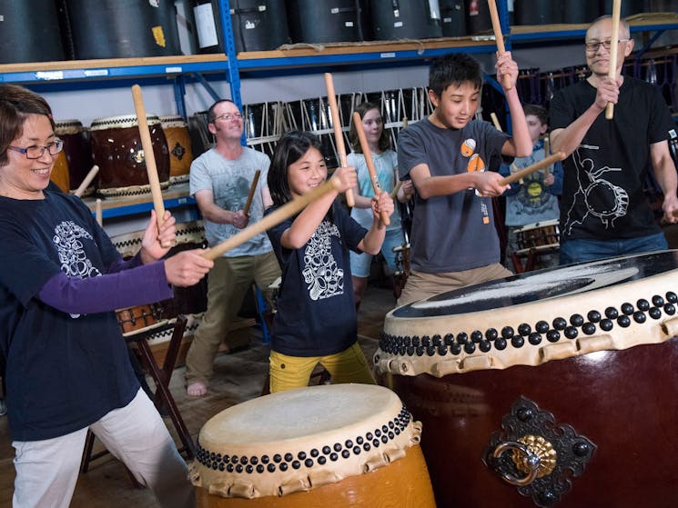 A family holding bachi sticks hit taiko drums