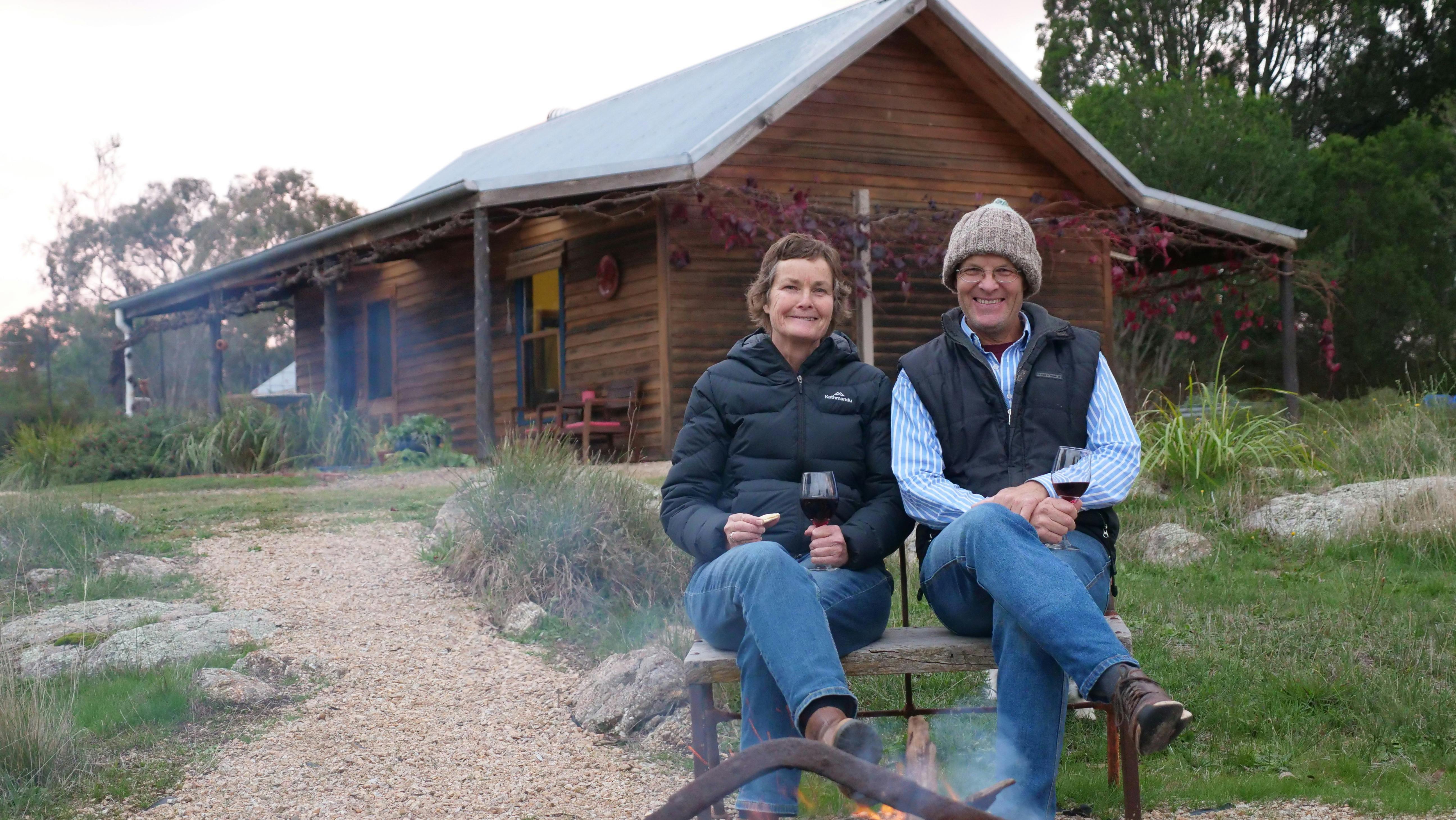 Two people sitting by a firepit with the retreat in the background sipping red wine