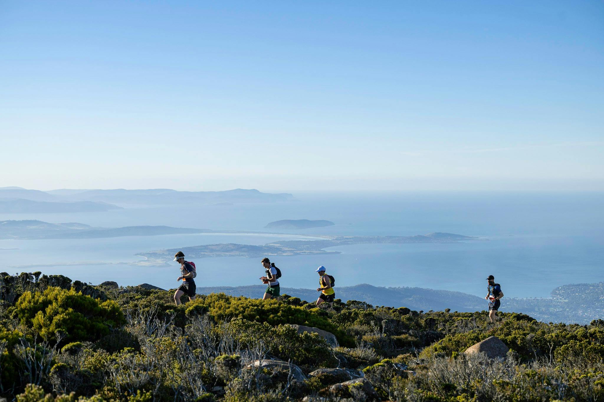 Four people running on a slight incline with the blue sky and Hobart dominant