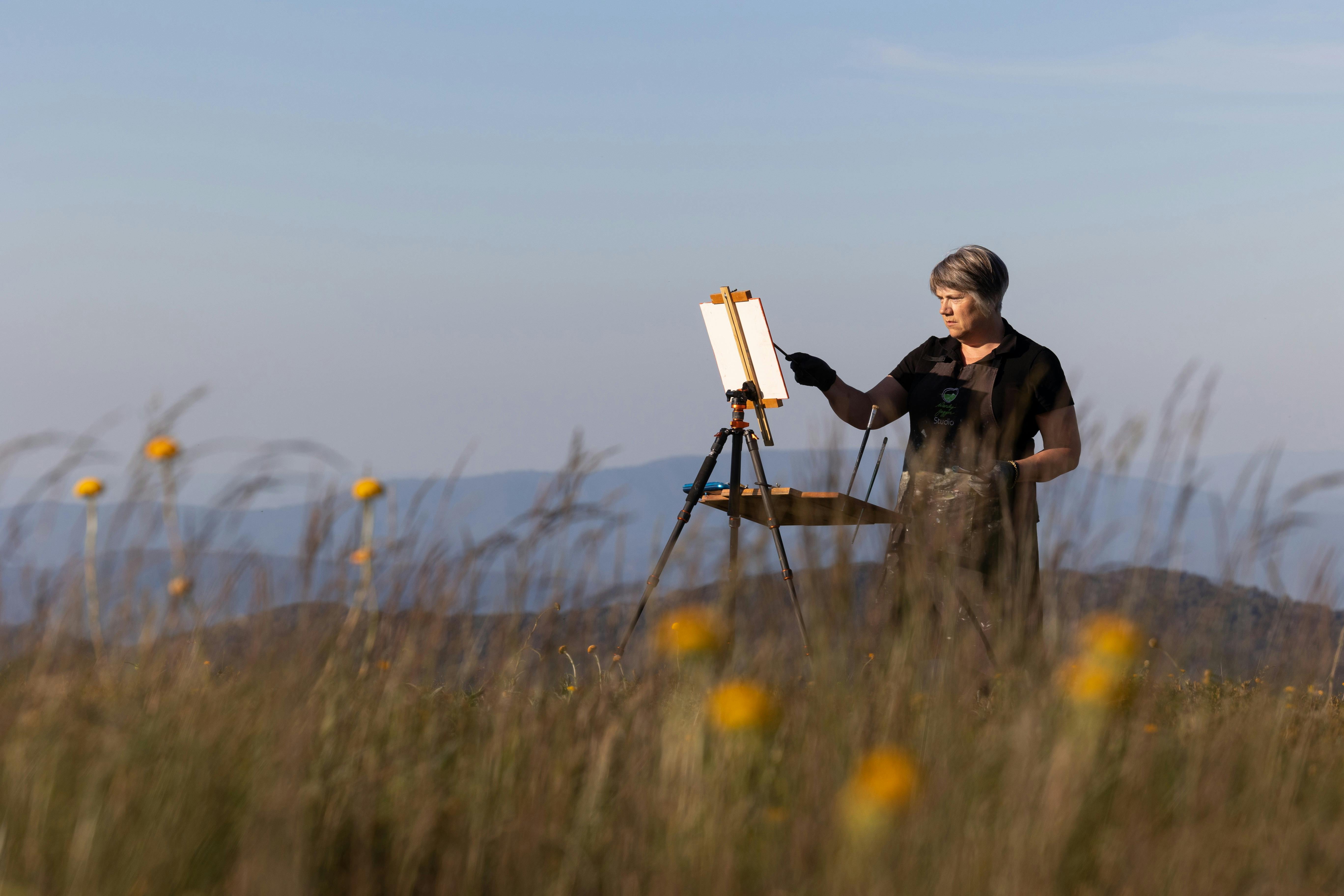 Painter among the wildflowers, mountains in the background.
