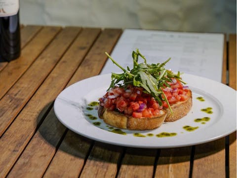 Tomato and onion bruchetta on crusty bread on a white plate with olive oil drizzled around it