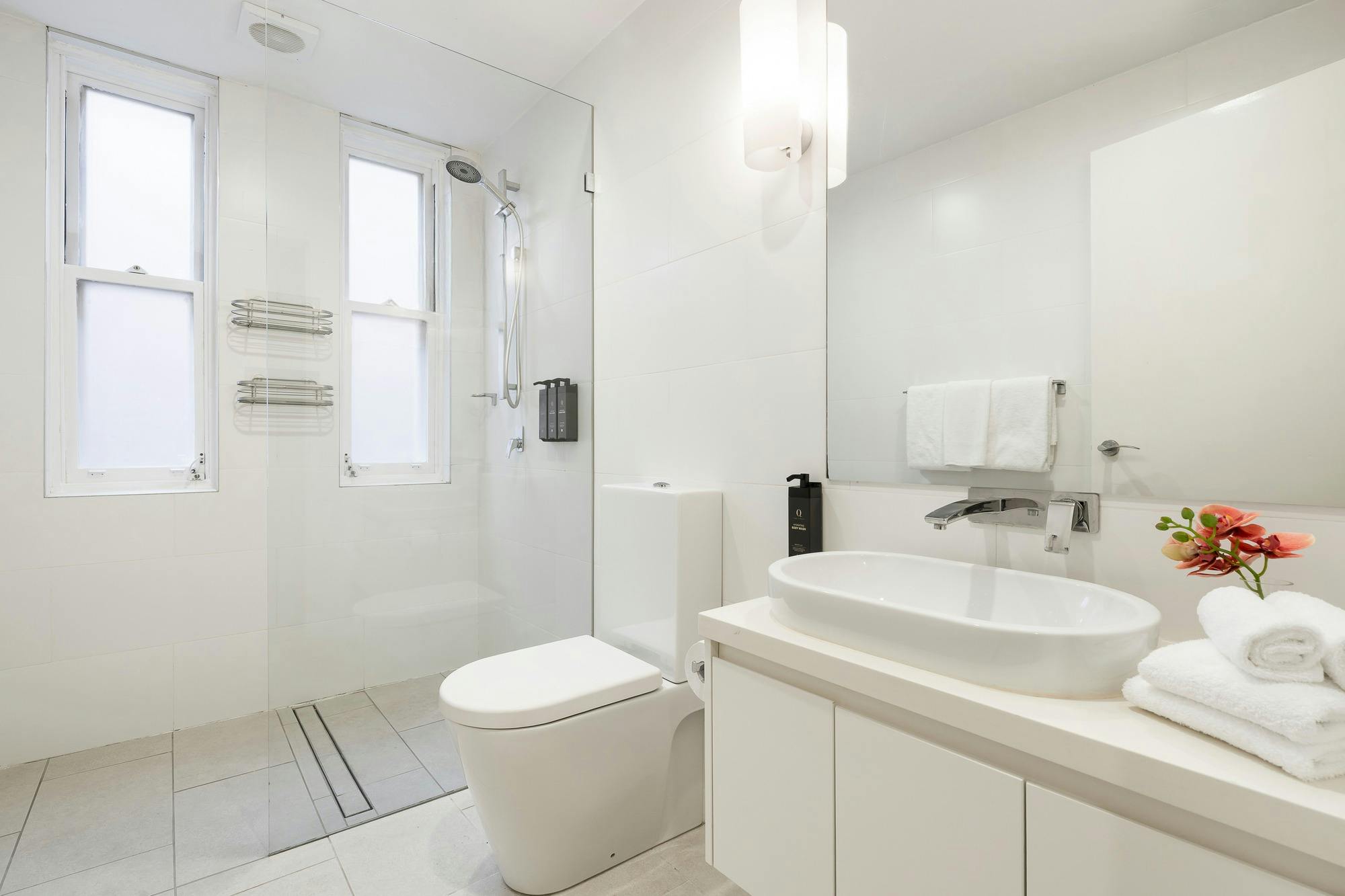Modern bathroom with large walk-in shower, toilet, large sink with mirror and white cabinetry.