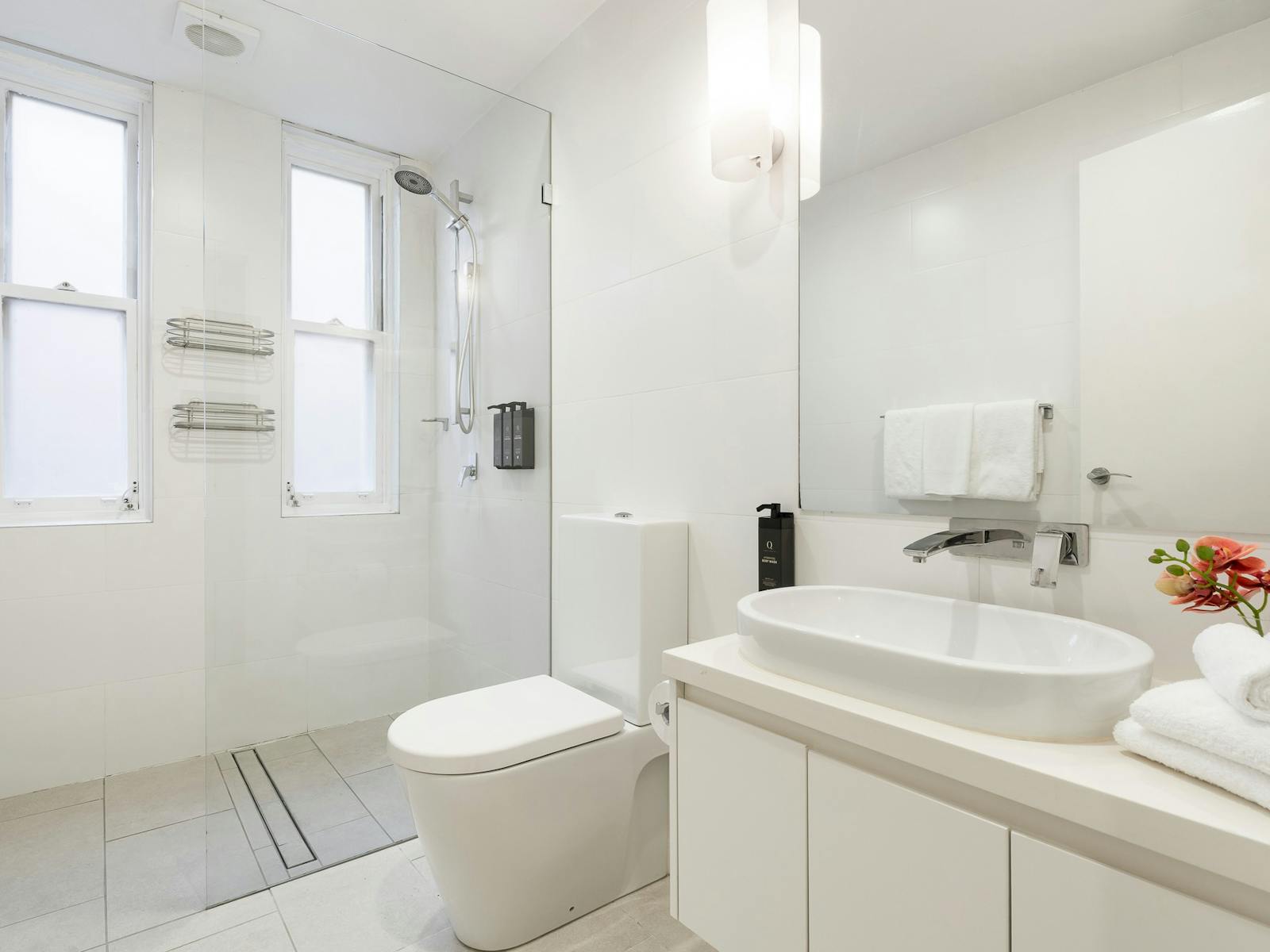 Modern bathroom with large walk-in shower, toilet, large sink with mirror and white cabinetry.