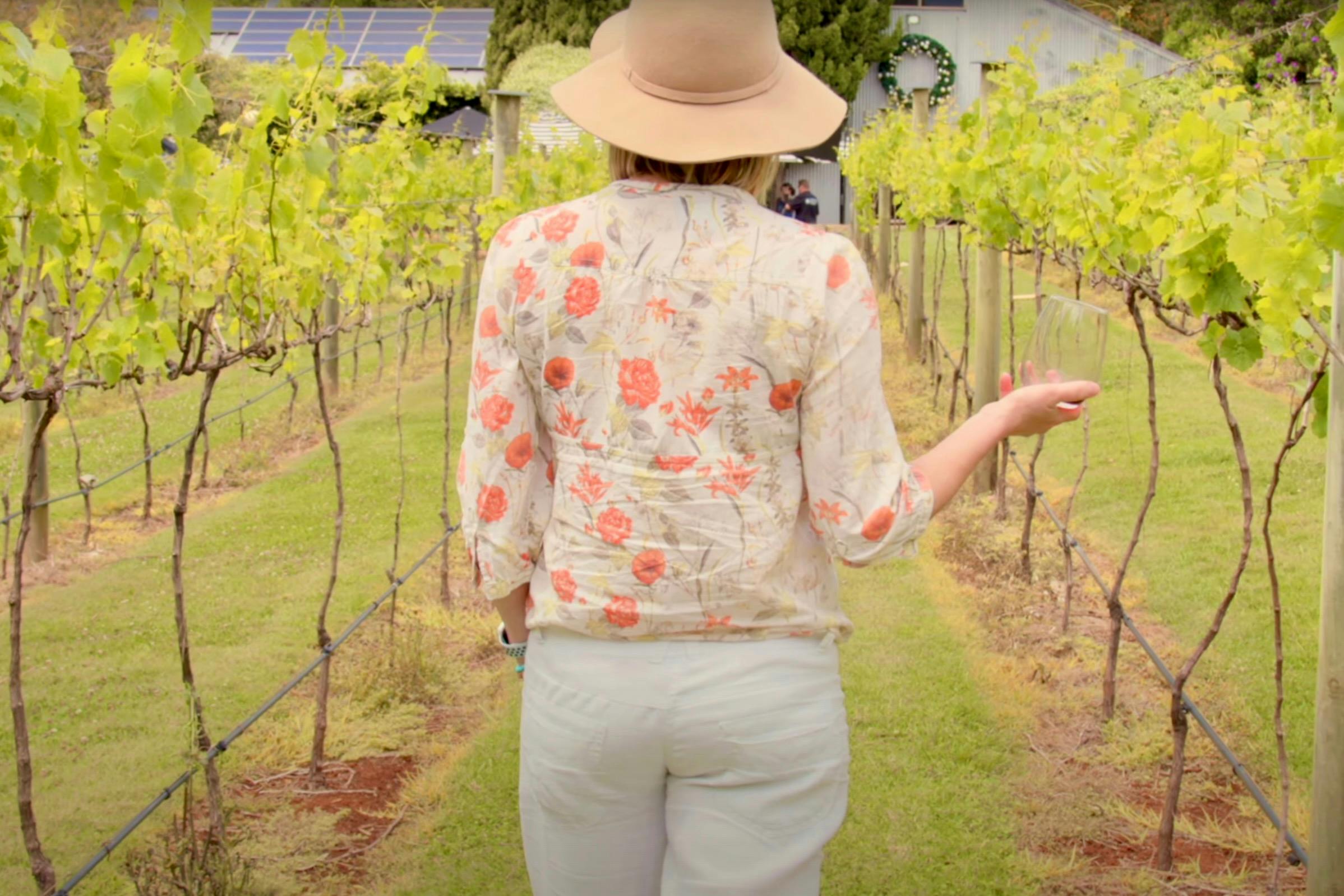 A women walking through the vineyard at Witches Falls Winery holding a glass of wine