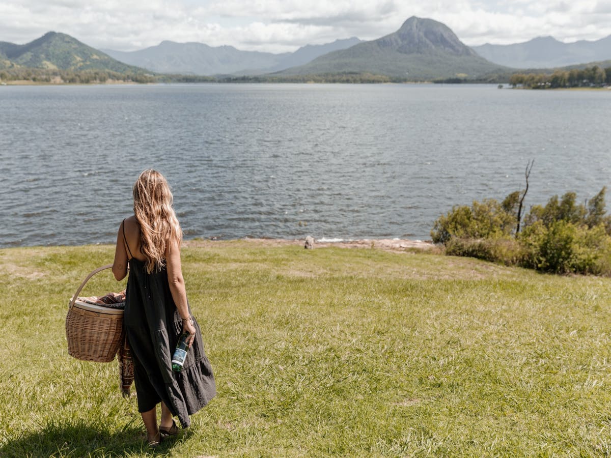 A woman walks towards the edge of a lake carrying a picnic basket