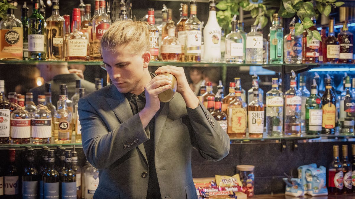 Man in a green suit shaking a cocktail behind a bar