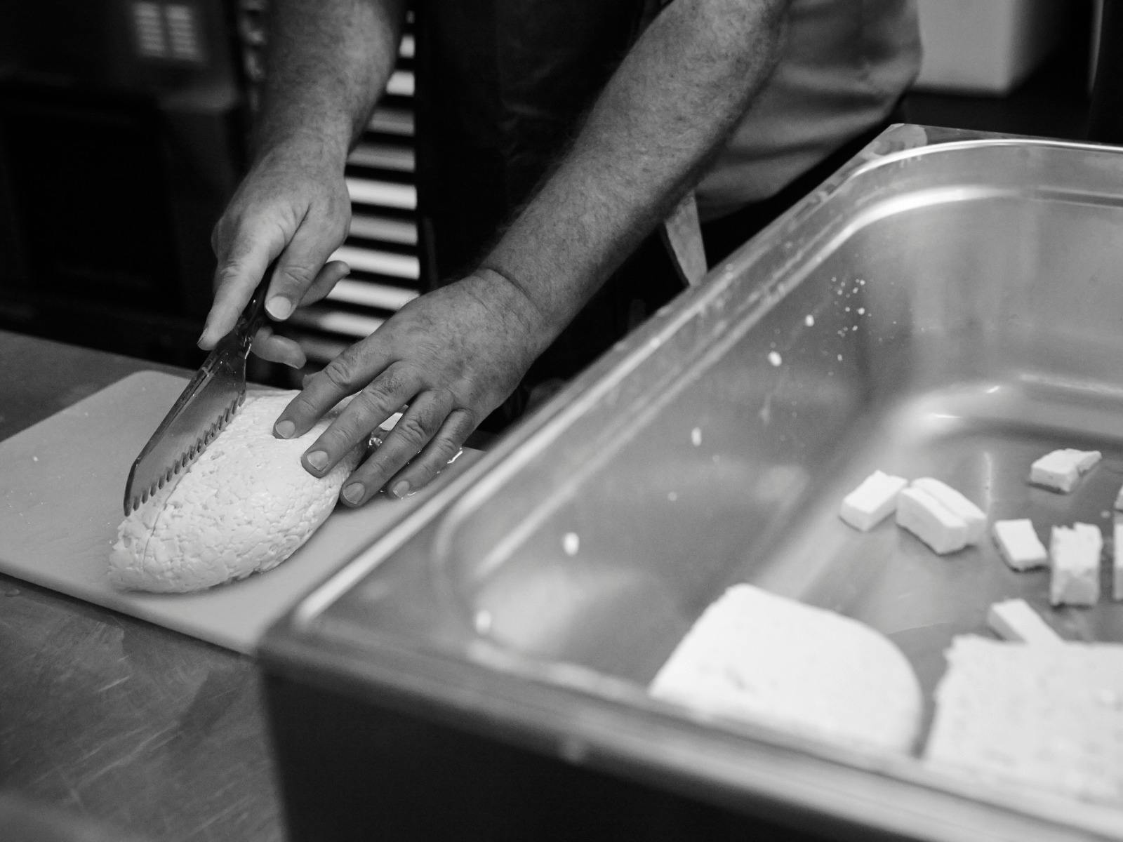 Hands slice a finished piece of cheese