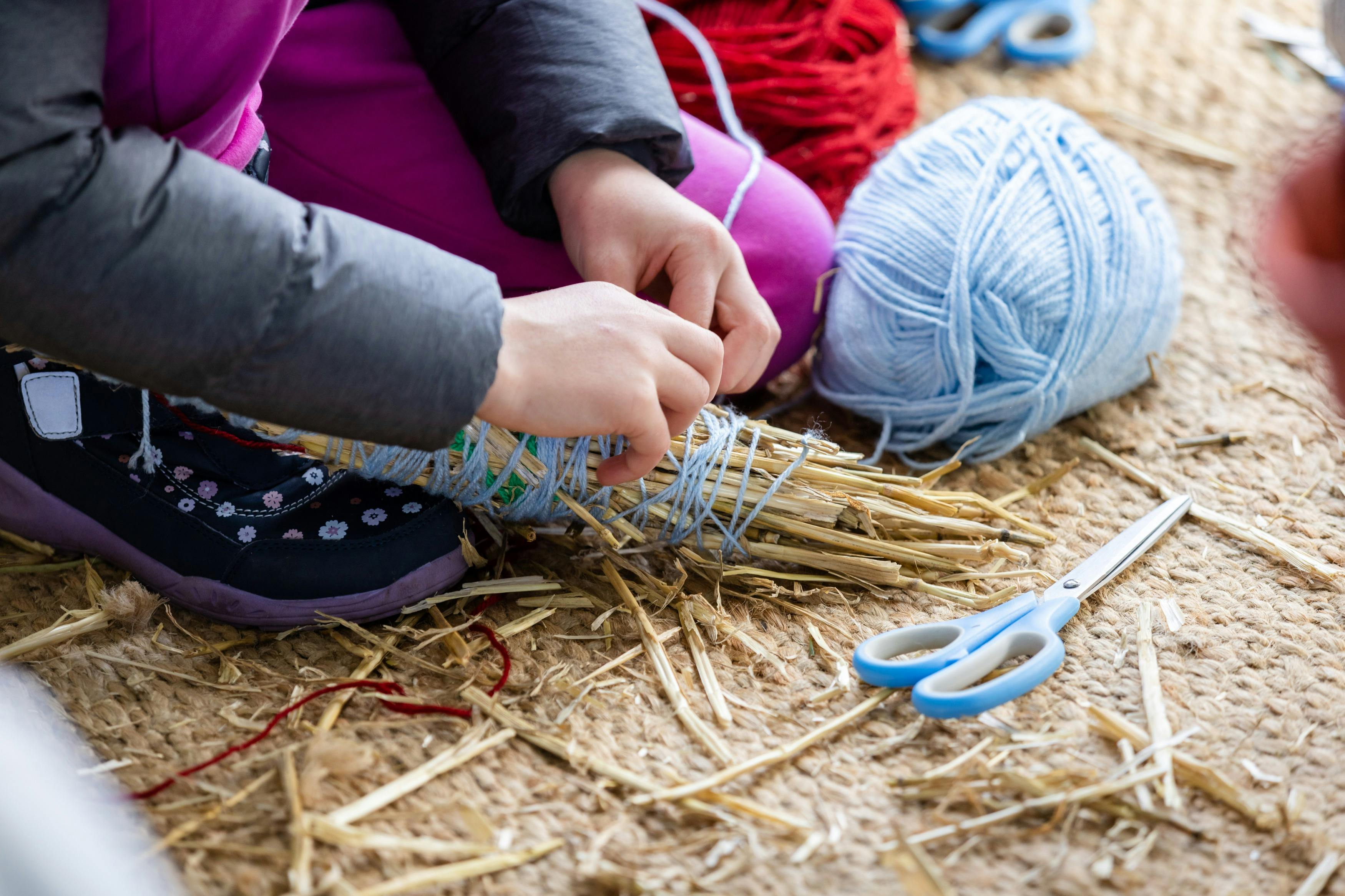 Person wrapping blue yarn around a bundle of straw