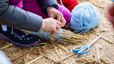 Person wrapping blue yarn around a bundle of straw