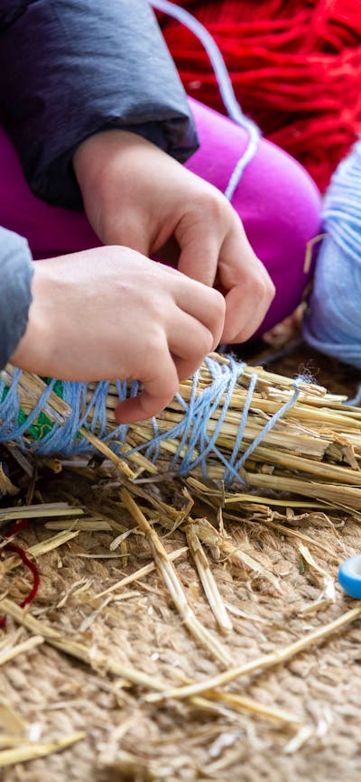 Person wrapping blue yarn around a bundle of straw