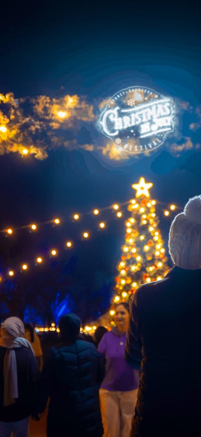 Woman standing in front of the festival's entry with Christmas lights and tree