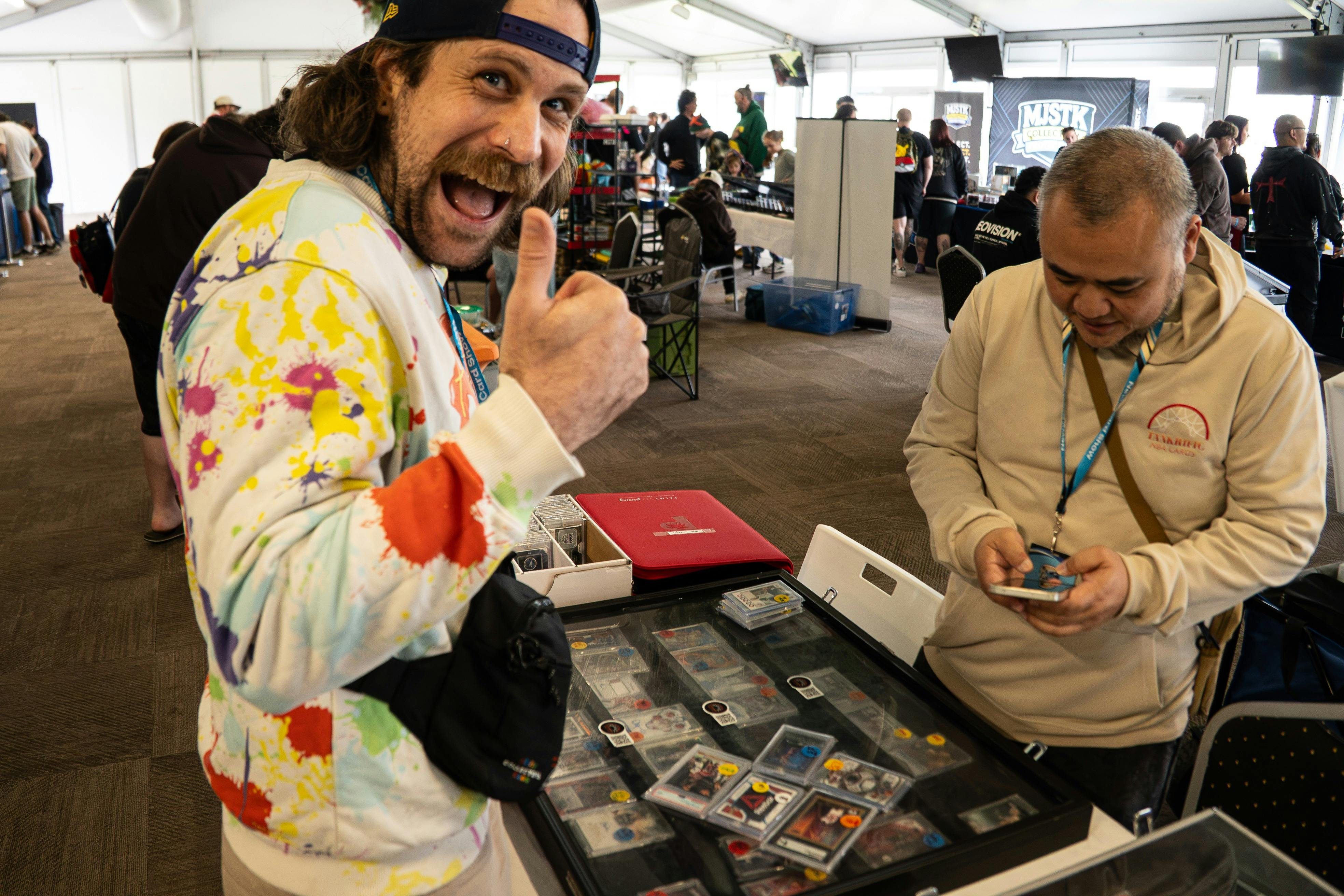 A vendor gives a thumbs-up beside a display of trading cards.