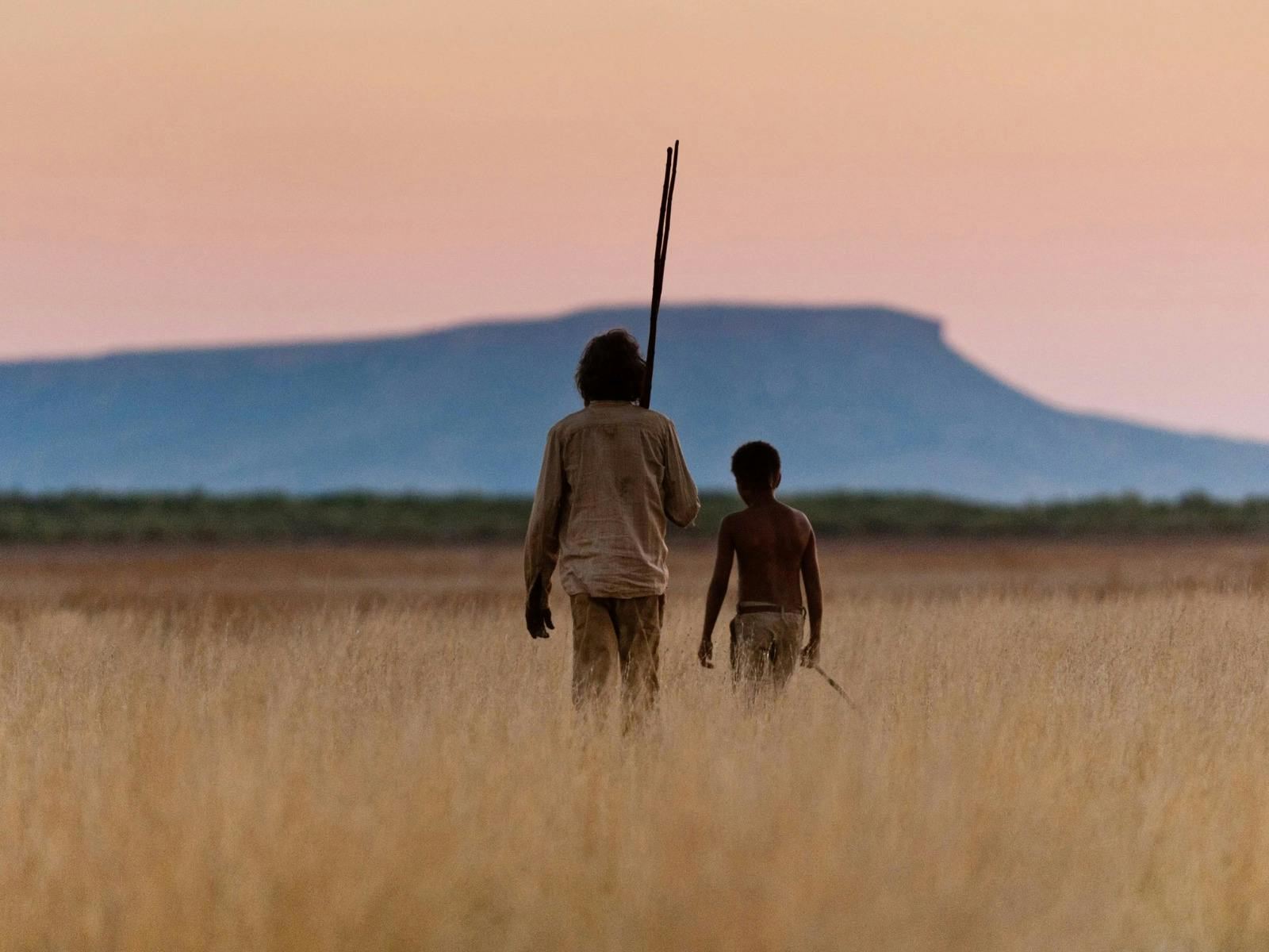 Older man and young boy walking through dry fields during sunset