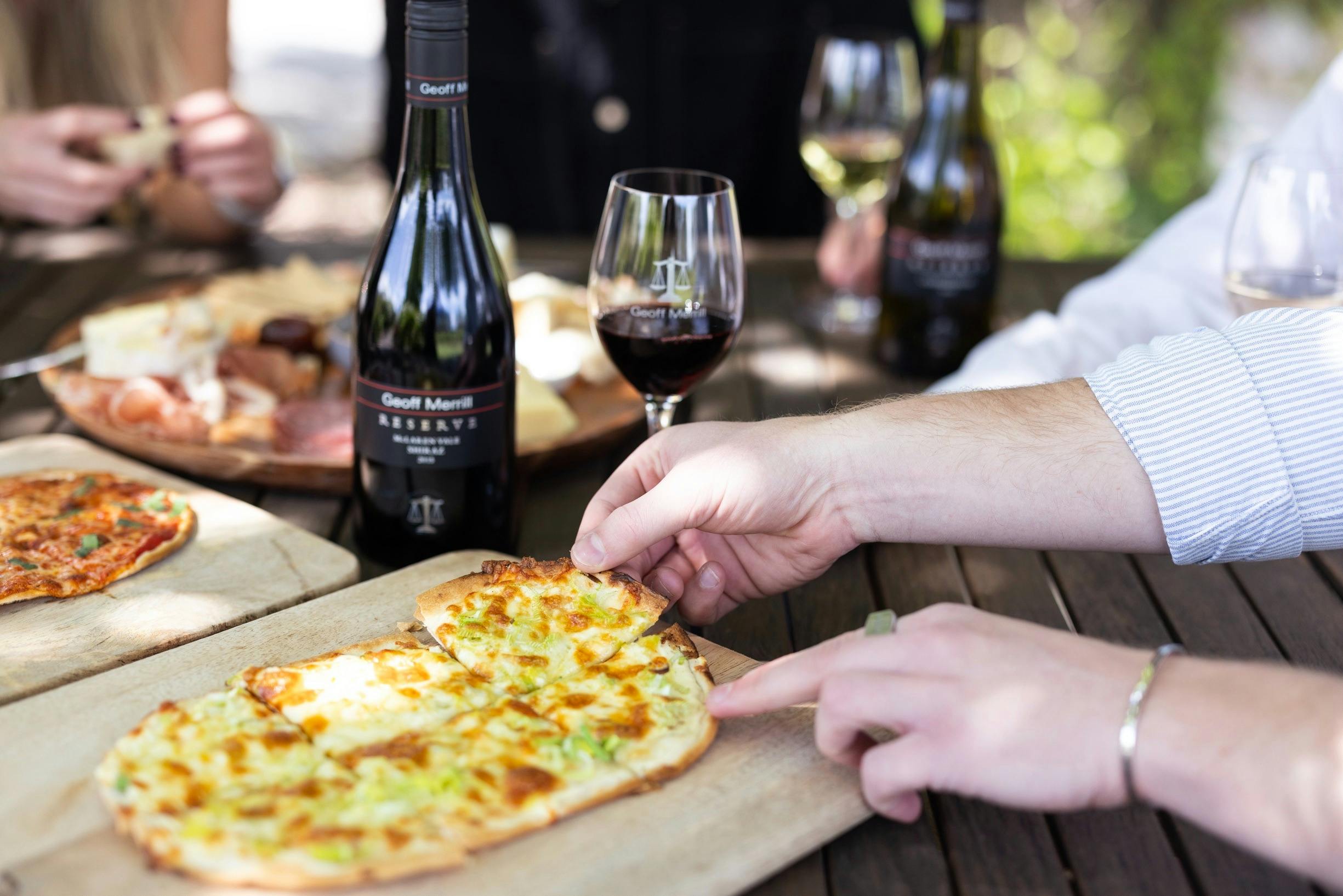 A hand reaching for a slice of pizza with red wine behind