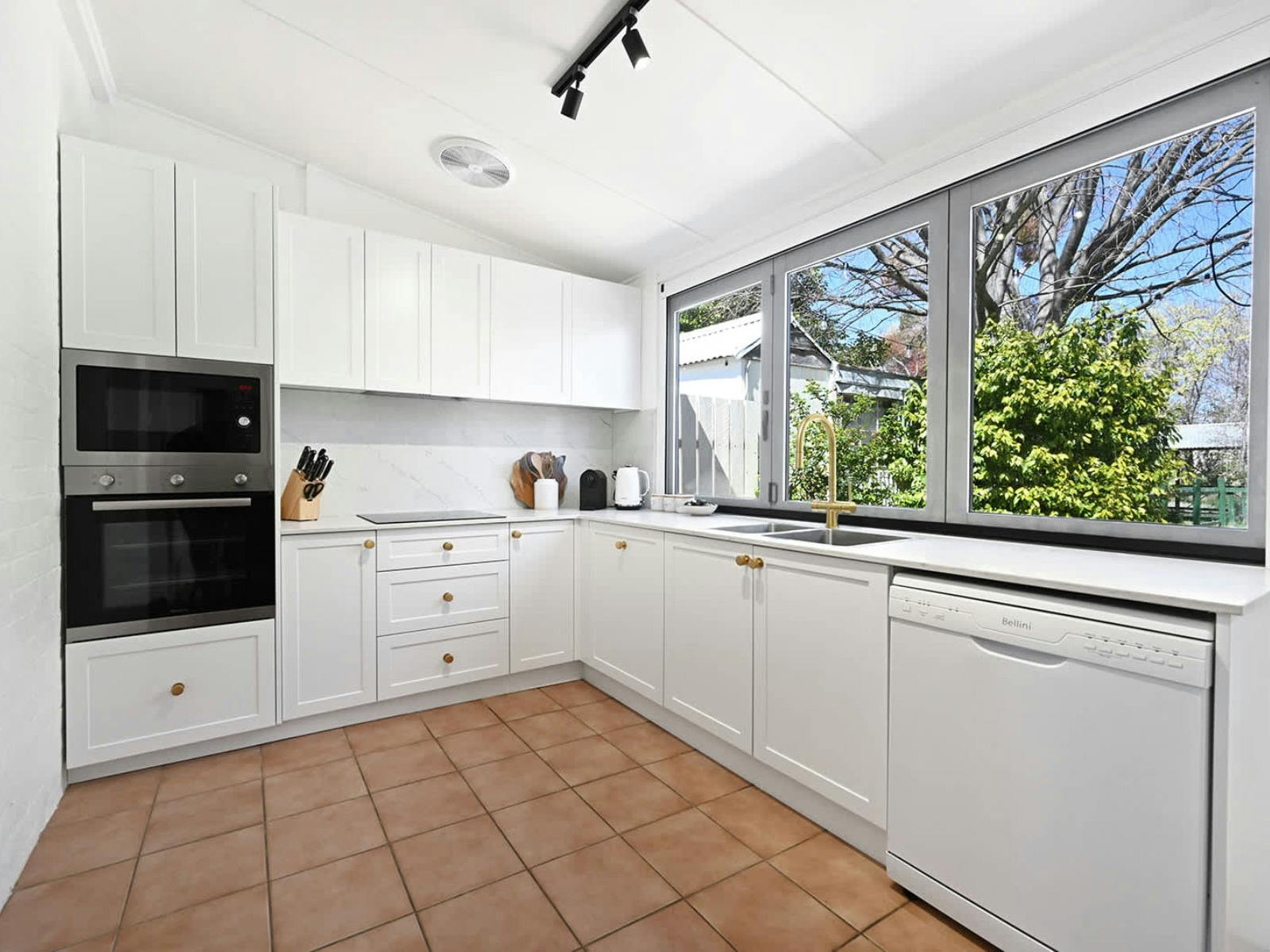 White kitchen cabinets with a large window to the backyard, dishwasher, oven and microwave
