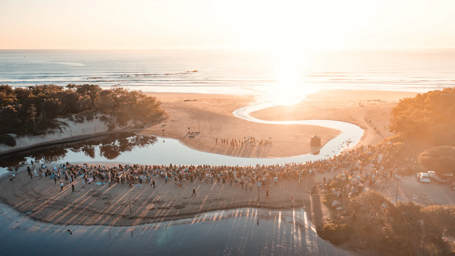 Aerial view of people gathered on a beach watching a performance at dawn