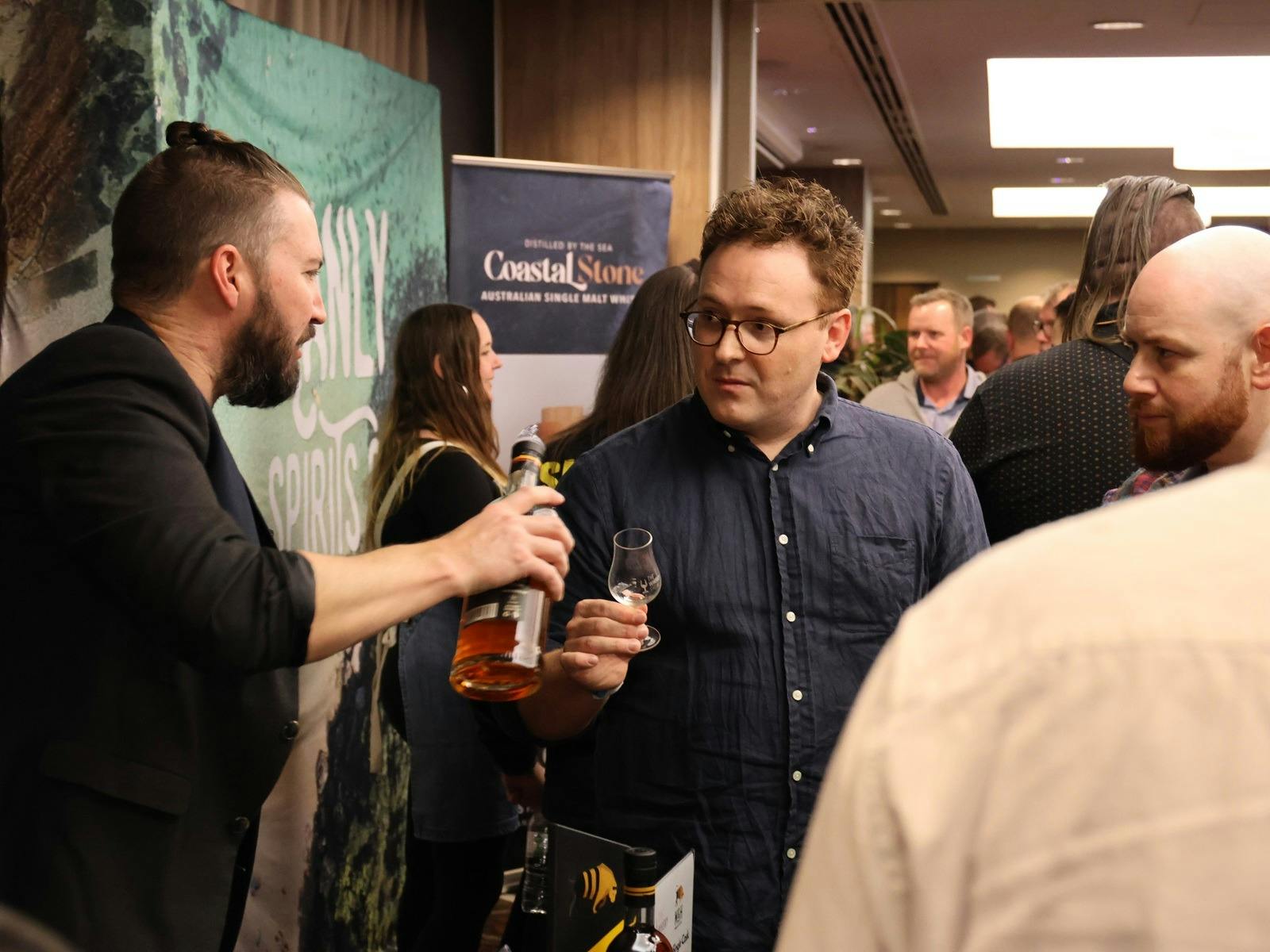Two people reach out for a sample of a whisky.